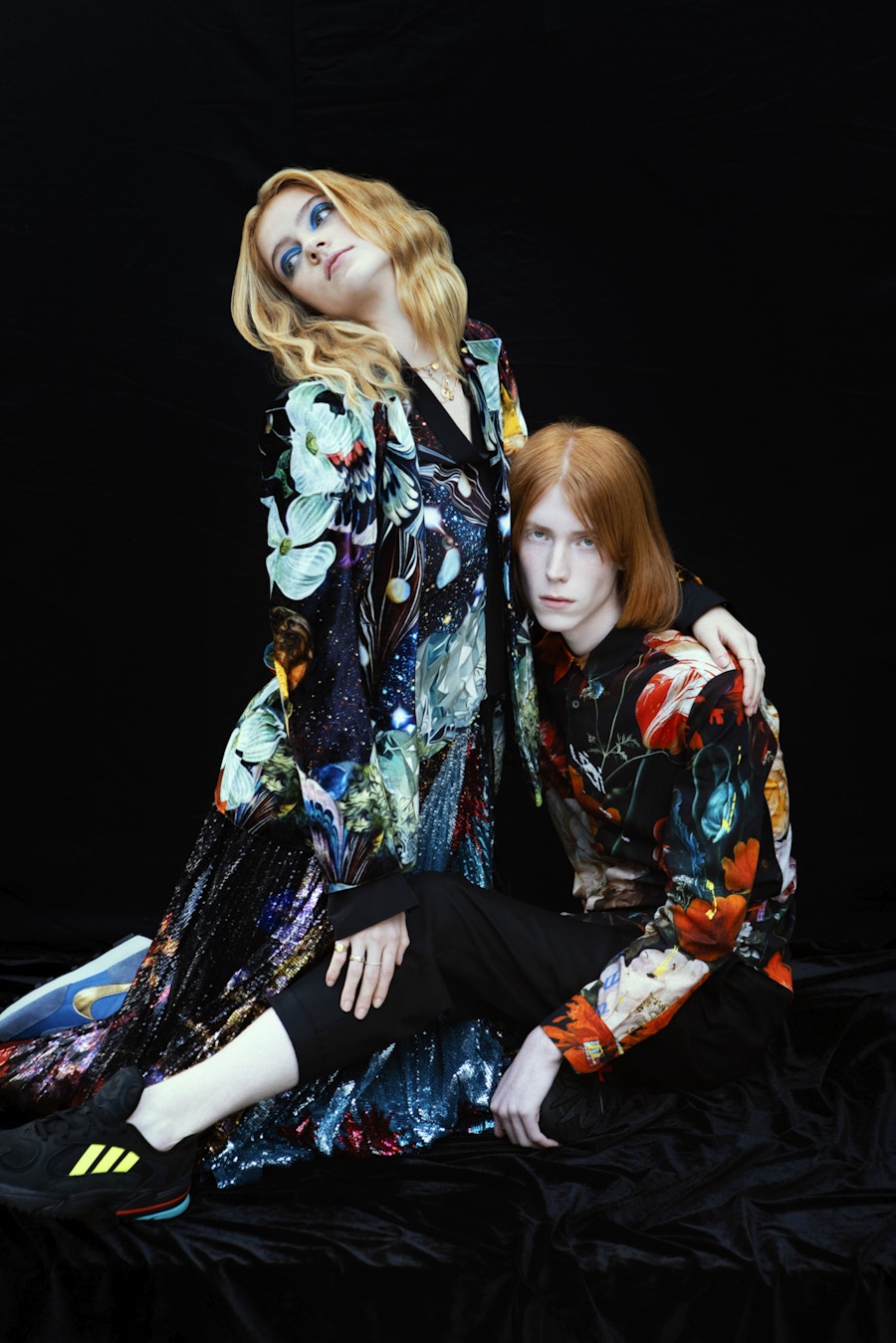 Two models wearing multi-coloured floral patterned clothes resting against each other