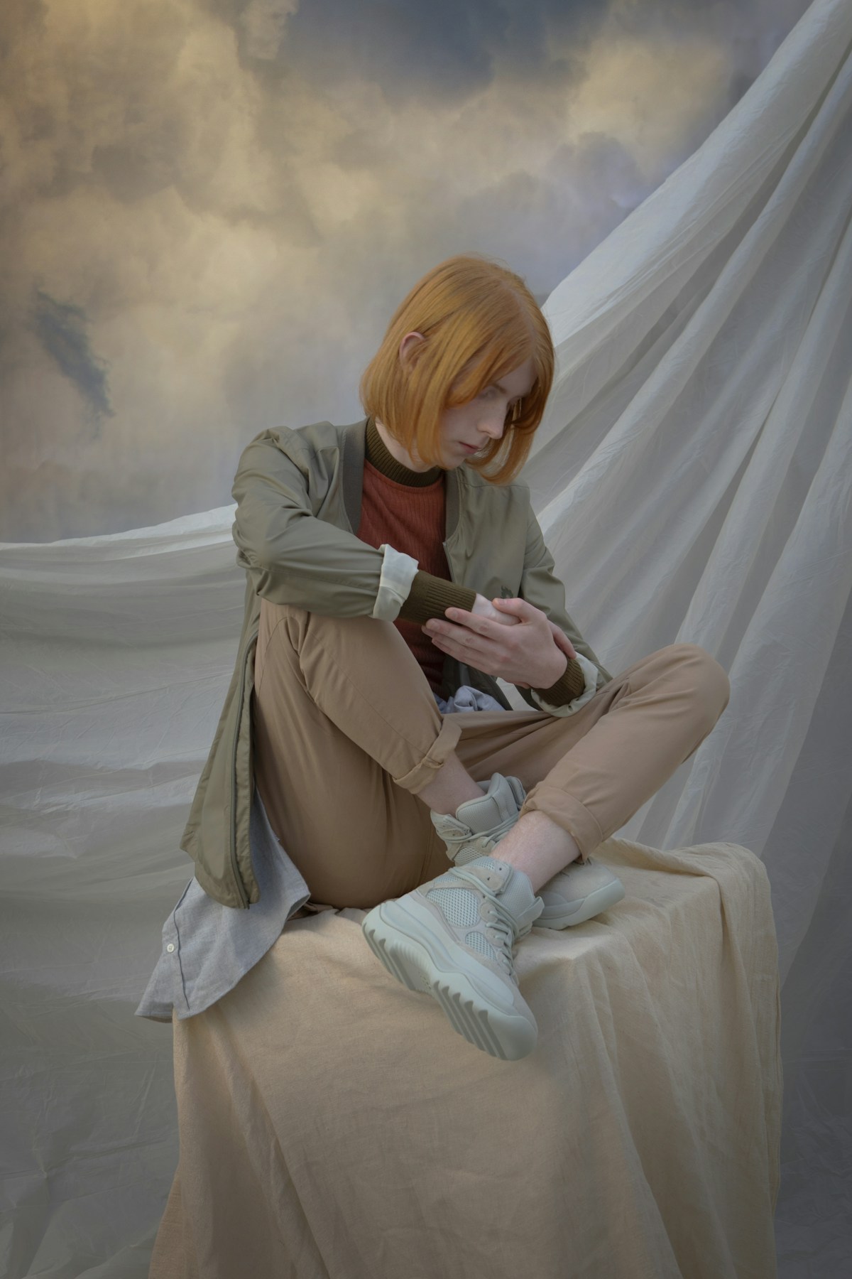 A model sitting on a cloth covered pedestal in front of a cloud background
