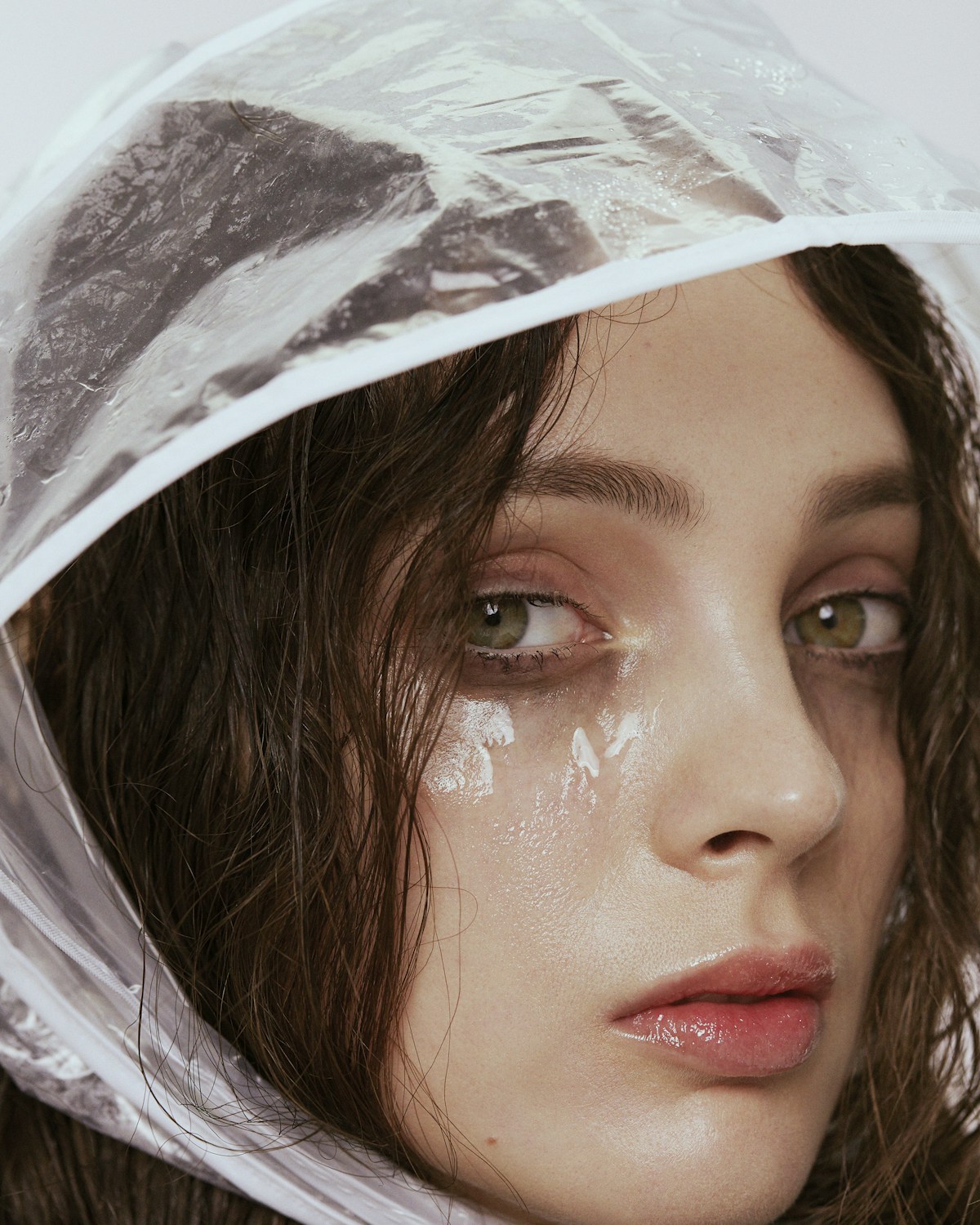 A woman wearing a clear plastic rain hood. Her eyes look watery