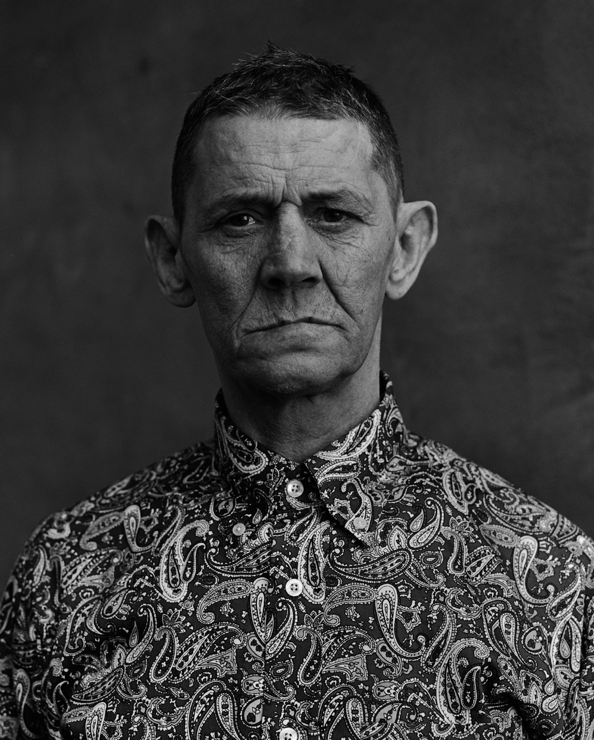 A man dressed in a patterned shirt stares at the camera.